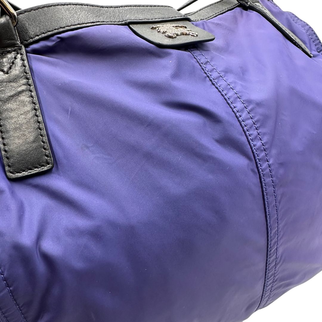 Borsa Burberry Tote Buckleigh in nylon viola con finiture in pelle nera e parti metalliche effetto renio. Munita di doppi manici, da indossare a spalla. Originale, usato, in condizioni ottime. 