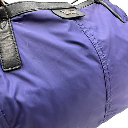 Borsa Burberry Tote Buckleigh in nylon viola con finiture in pelle nera e parti metalliche effetto renio. Munita di doppi manici, da indossare a spalla. Originale, usato, in condizioni ottime. 