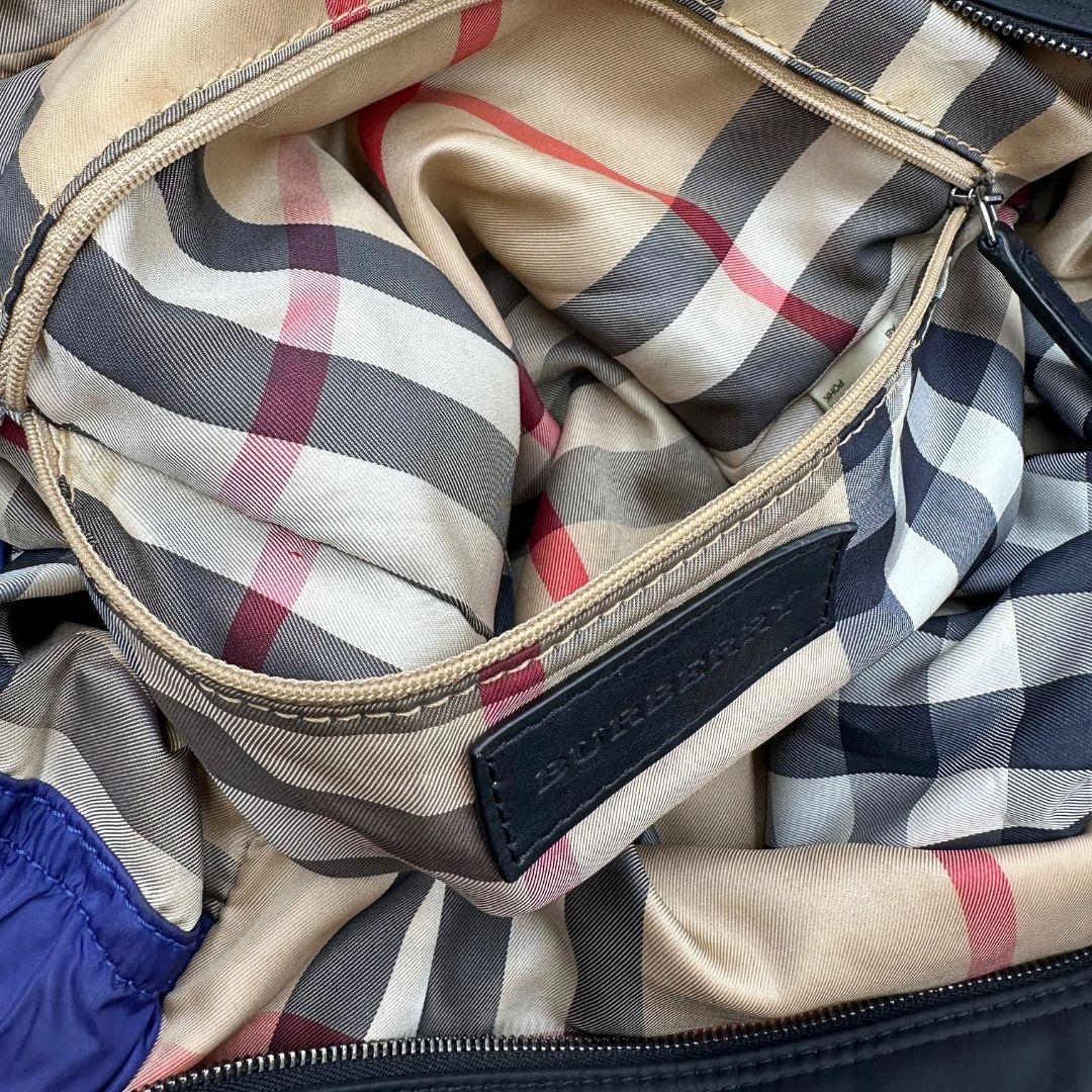 Borsa Burberry Tote Buckleigh in nylon viola con finiture in pelle nera e parti metalliche effetto renio. Munita di doppi manici, da indossare a spalla. Originale, usato, in condizioni ottime. 