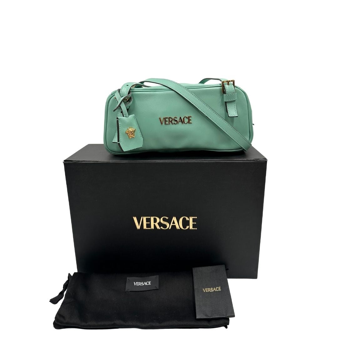 Bauletto Versace in pelle verde tiffany con parti metalliche dorate e doppi manici leggermente regolabili. Rifinita con logo lettering sul front e medusa sulla clochette rimovibile. Completo di corredo. Originale, usato, in condizioni ottime. 