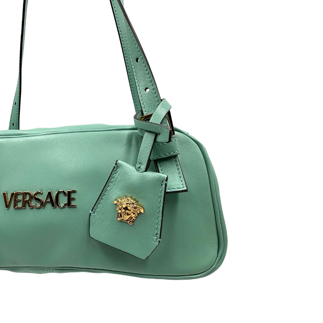 Bauletto Versace in pelle verde tiffany con parti metalliche dorate e doppi manici leggermente regolabili. Rifinita con logo lettering sul front e medusa sulla clochette rimovibile. Completo di corredo. Originale, usato, in condizioni ottime. 