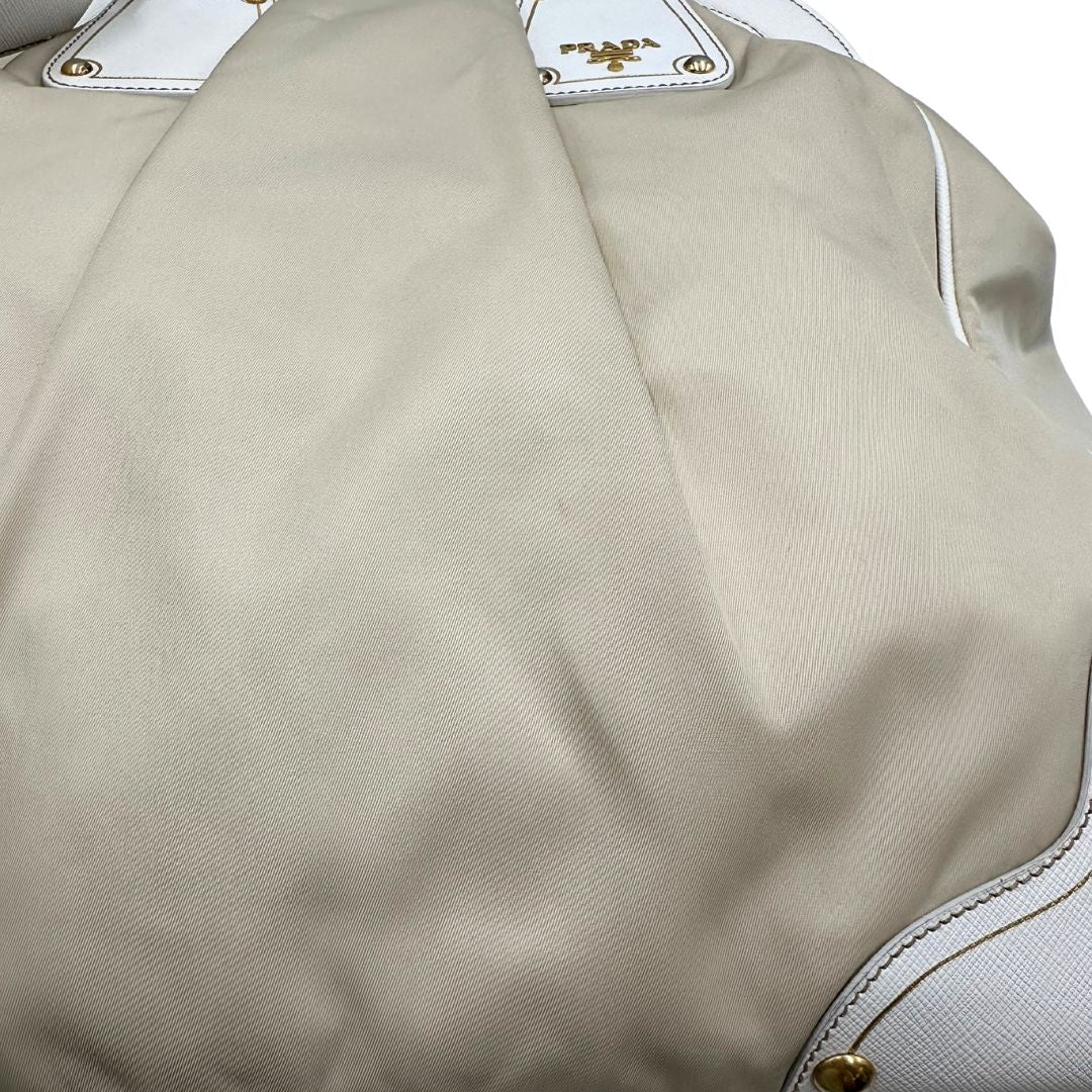 Borsa Tote Prada in nylon bianco panna con finiture in pelle bianco gesso e parti metalliche dorate. Munita di doppi manici stondati con tag porta address rimovibile. Rifinita con logo lettering al di sotto del manico. Originale, usato, in condizioni ottime. 