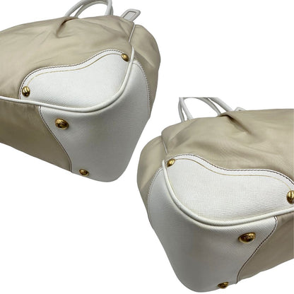Angoli Borsa Tote Prada in nylon bianco panna con finiture in pelle bianco gesso e parti metalliche dorate. Munita di doppi manici stondati con tag porta address rimovibile. Rifinita con logo lettering al di sotto del manico. Originale, usato, in condizioni ottime. 