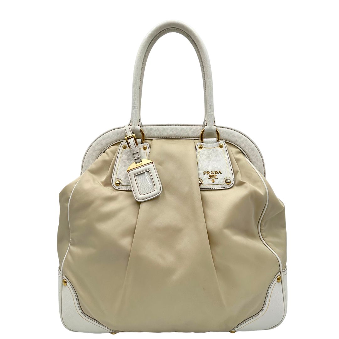 Borsa Tote Prada in nylon bianco panna con finiture in pelle bianco gesso e parti metalliche dorate. Munita di doppi manici stondati con tag porta address rimovibile. Rifinita con logo lettering al di sotto del manico. Originale, usato, in condizioni ottime. 