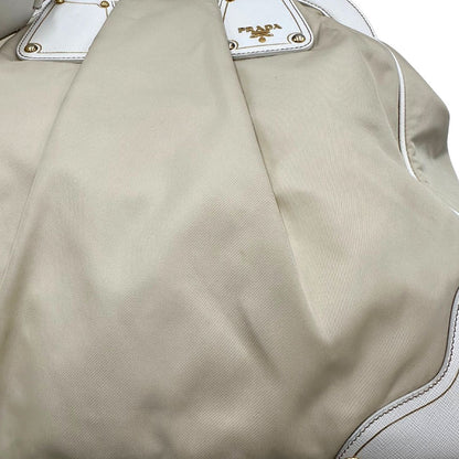 Borsa Tote Prada in nylon bianco panna con finiture in pelle bianco gesso e parti metalliche dorate. Munita di doppi manici stondati con tag porta address rimovibile. Rifinita con logo lettering al di sotto del manico. Originale, usato, in condizioni ottime. 