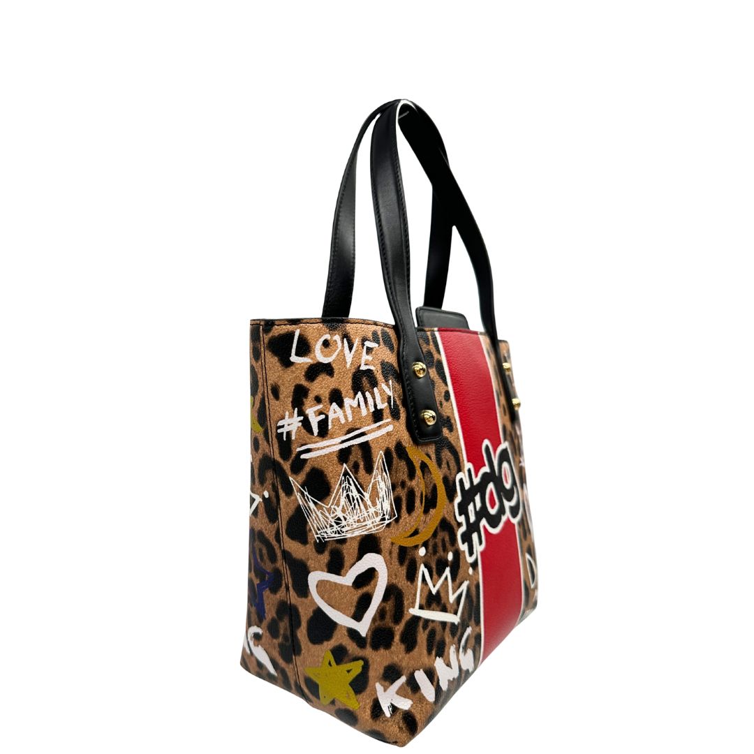 Borsa D&G tote Beatrice in canvas con motivo animalier e dettagli graffiti in stile street-art. Il design è arricchito da scritte, cuori e corone, e impreziosita da una striscia centrale rossa. Presenta doppi manici in pelle nera e parti metalliche dorate. Completa di dustbag, cartellino e card d'autenticità. Originale, usato, in condizioni ottime. 