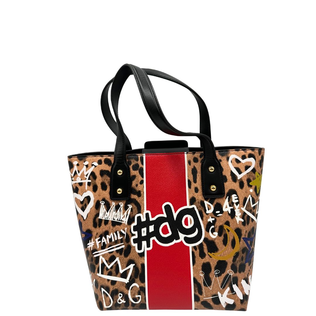 Retro Borsa D&G tote Beatrice in canvas con motivo animalier e dettagli graffiti in stile street-art. Il design è arricchito da scritte, cuori e corone, e impreziosita da una striscia centrale rossa. Presenta doppi manici in pelle nera e parti metalliche dorate. Completa di dustbag, cartellino e card d'autenticità. Originale, usato, in condizioni ottime. 