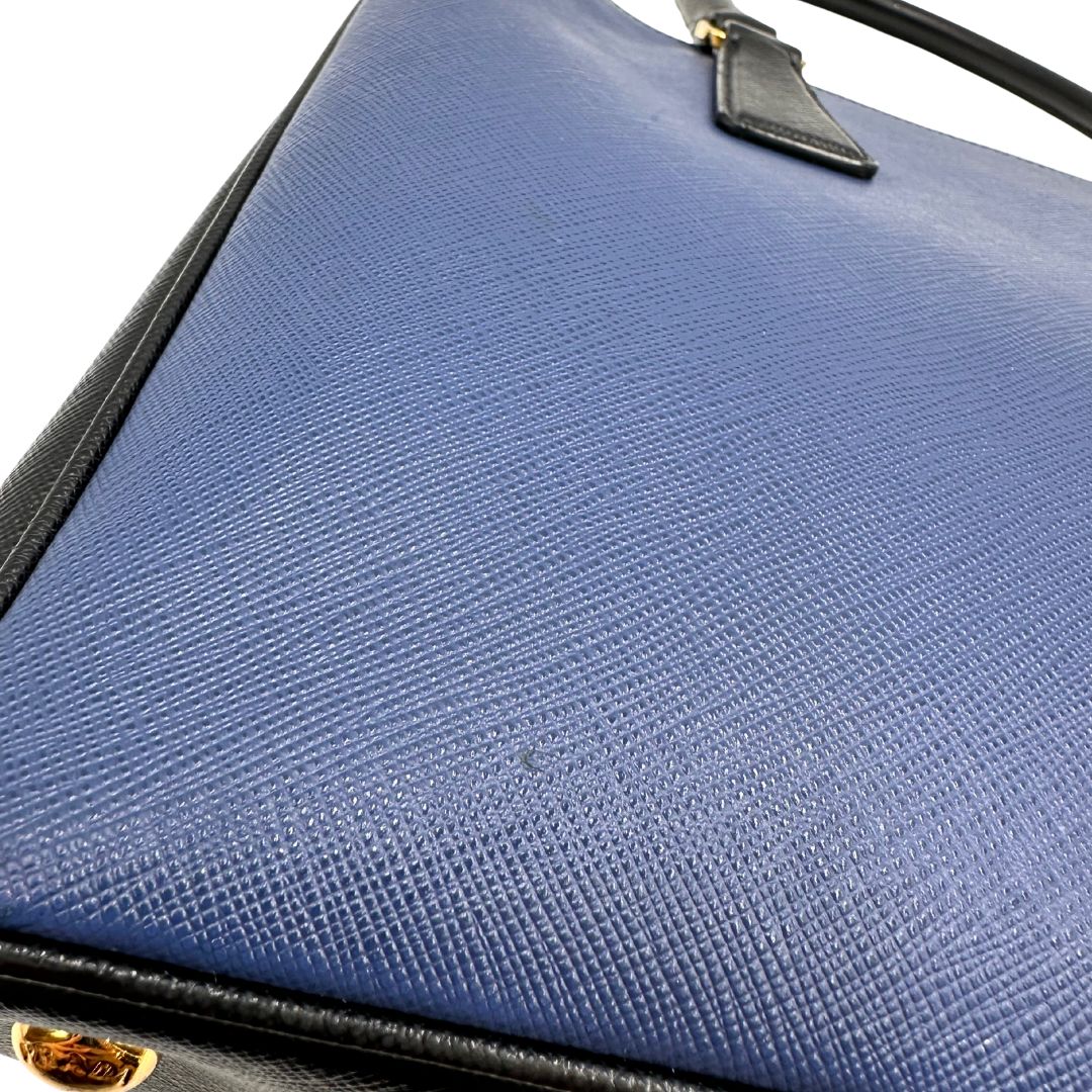 Borsa Prada in pelle saffiano blu e nera con parti metalliche dorate; munita di doppi manici stondati e impreziosita da un portachiavi. Completa di dustbag, di lusso, originale, ottime condizoni, usata. 