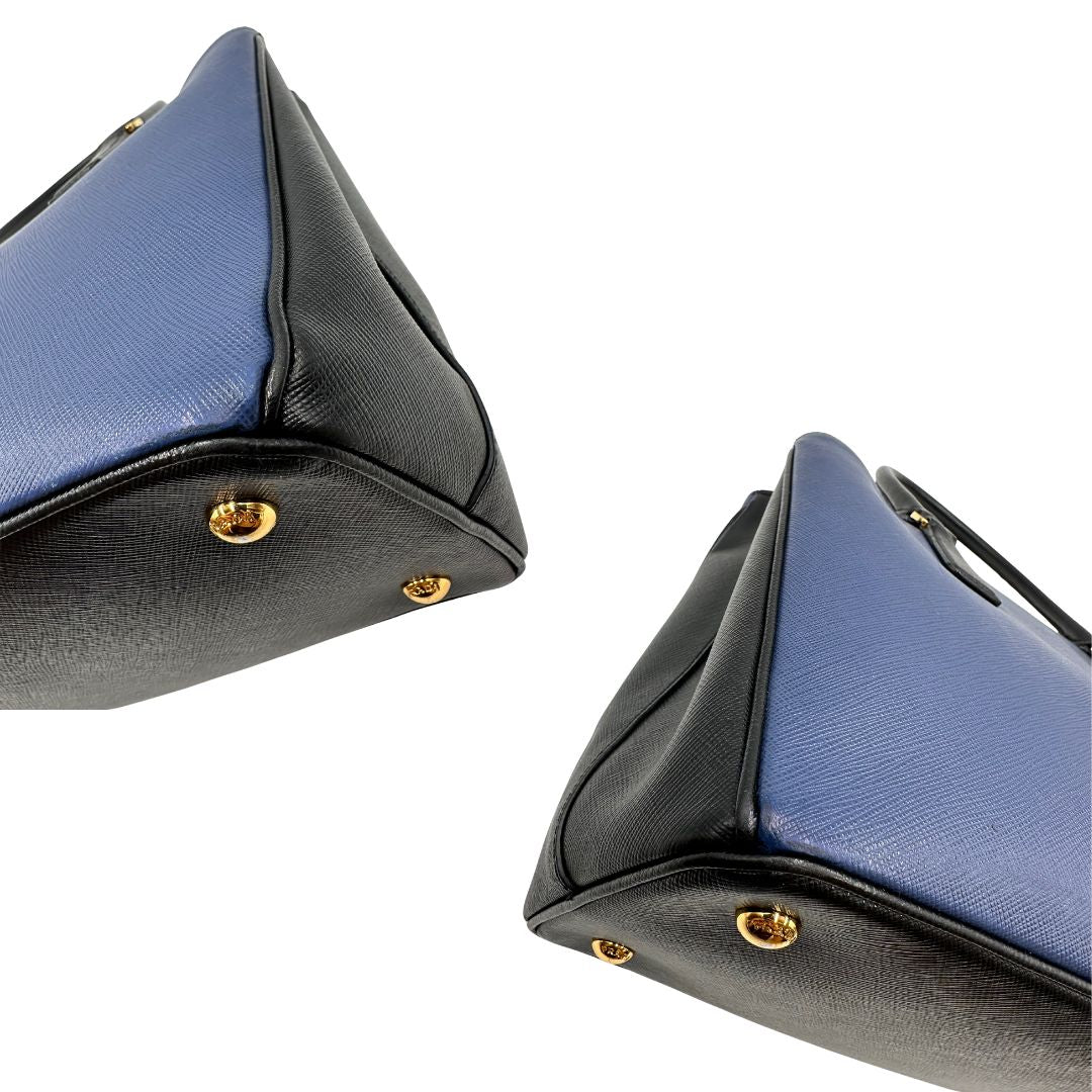 angoli Borsa Prada in pelle saffiano blu e nera con parti metalliche dorate; munita di doppi manici stondati e impreziosita da un portachiavi. Completa di dustbag, di lusso, originale, ottime condizoni, usata. 