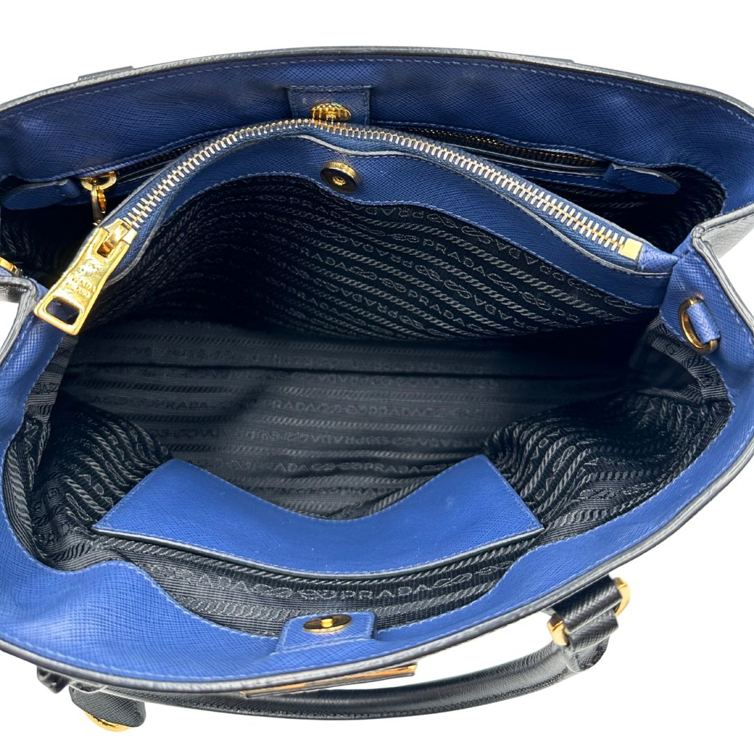 interno Borsa Prada in pelle saffiano blu e nera con parti metalliche dorate; munita di doppi manici stondati e impreziosita da un portachiavi. Completa di dustbag, di lusso, originale, ottime condizoni, usata. 