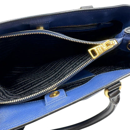 interno Borsa Prada in pelle saffiano blu e nera con parti metalliche dorate; munita di doppi manici stondati e impreziosita da un portachiavi. Completa di dustbag, di lusso, originale, ottime condizoni, usata. 