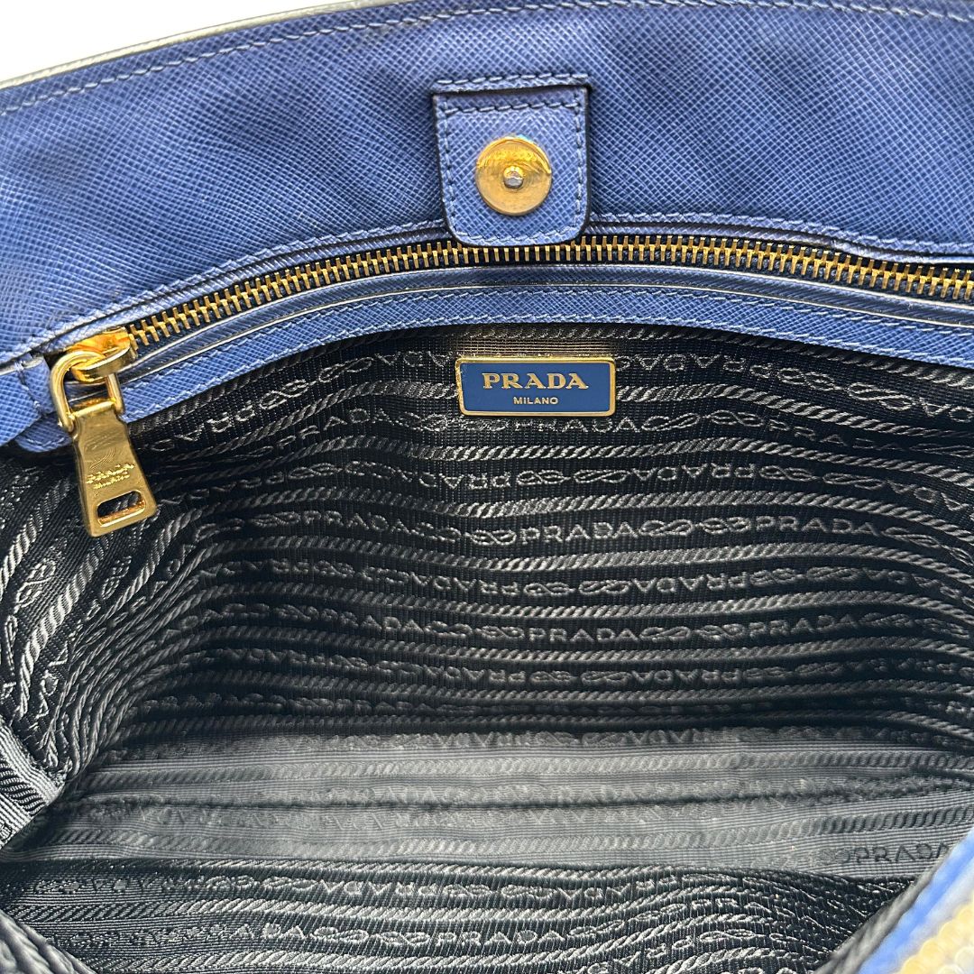 interno Borsa Prada in pelle saffiano blu e nera con parti metalliche dorate; munita di doppi manici stondati e impreziosita da un portachiavi. Completa di dustbag, di lusso, originale, ottime condizoni, usata. 