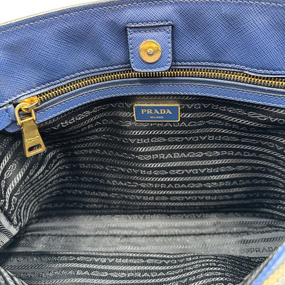 interno Borsa Prada in pelle saffiano blu e nera con parti metalliche dorate; munita di doppi manici stondati e impreziosita da un portachiavi. Completa di dustbag, di lusso, originale, ottime condizoni, usata. 