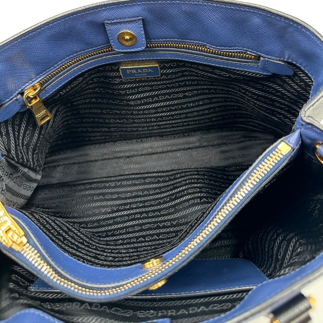 interno Borsa Prada in pelle saffiano blu e nera con parti metalliche dorate; munita di doppi manici stondati e impreziosita da un portachiavi. Completa di dustbag, di lusso, originale, ottime condizoni, usata. 