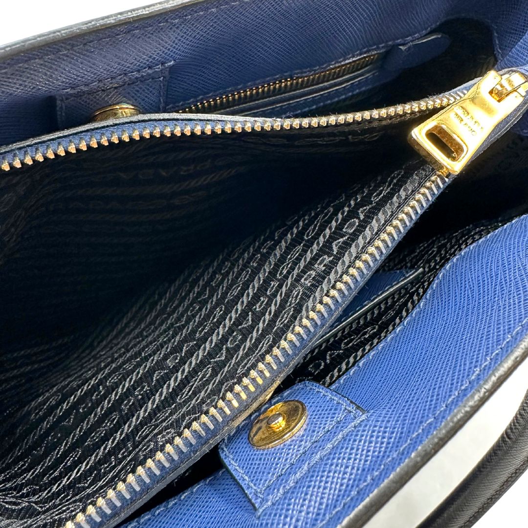 interno Borsa Prada in pelle saffiano blu e nera con parti metalliche dorate; munita di doppi manici stondati e impreziosita da un portachiavi. Completa di dustbag, di lusso, originale, ottime condizoni, usata. 