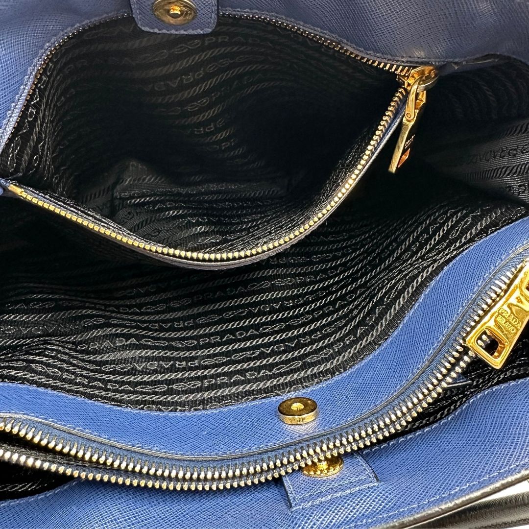 interno Borsa Prada in pelle saffiano blu e nera con parti metalliche dorate; munita di doppi manici stondati e impreziosita da un portachiavi. Completa di dustbag, di lusso, originale, ottime condizoni, usata. 