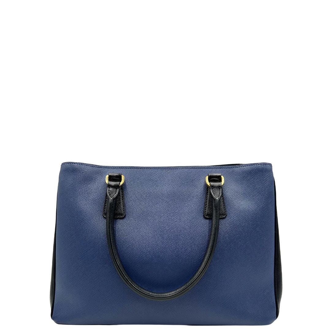 retro Borsa Prada in pelle saffiano blu e nera con parti metalliche dorate; munita di doppi manici stondati e impreziosita da un portachiavi. Completa di dustbag, di lusso, originale, ottime condizoni, usata. 
