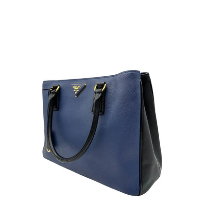 lato Borsa Prada in pelle saffiano blu e nera con parti metalliche dorate; munita di doppi manici stondati e impreziosita da un portachiavi. Completa di dustbag, di lusso, originale, ottime condizoni, usata. 