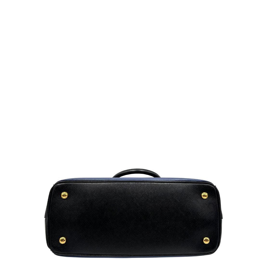 base Borsa Prada in pelle saffiano blu e nera con parti metalliche dorate; munita di doppi manici stondati e impreziosita da un portachiavi. Completa di dustbag, di lusso, originale, ottime condizoni, usata. 