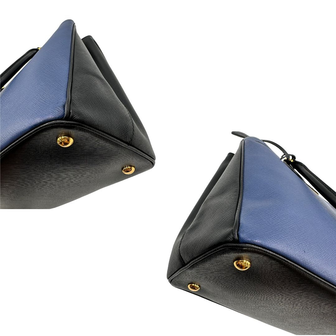 angoli Borsa Prada in pelle saffiano blu e nera con parti metalliche dorate; munita di doppi manici stondati e impreziosita da un portachiavi. Completa di dustbag, di lusso, originale, ottime condizoni, usata. 