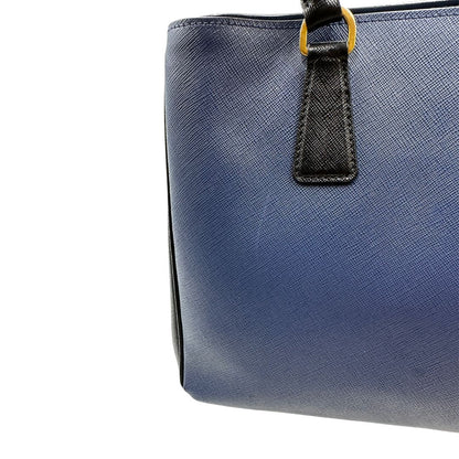 lato Borsa Prada in pelle saffiano blu e nera con parti metalliche dorate; munita di doppi manici stondati e impreziosita da un portachiavi. Completa di dustbag, di lusso, originale, ottime condizoni, usata. 