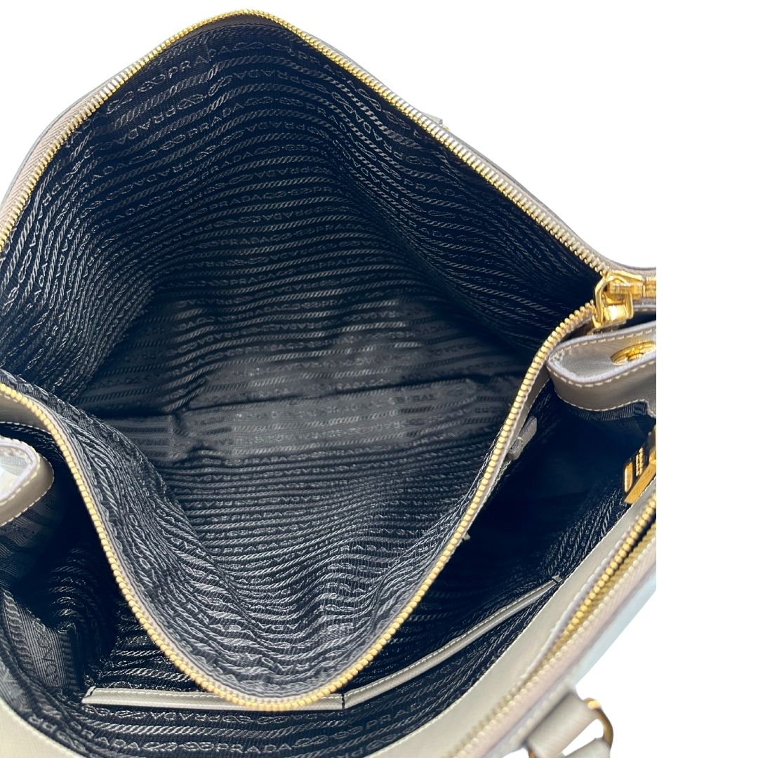 borsa Prada in pelle saffiano color fango con parti metalliche dorate; munita di doppi manici stondati e impreziosita da una clochette portachiavi, di lusso, originale, ottime condizioni.