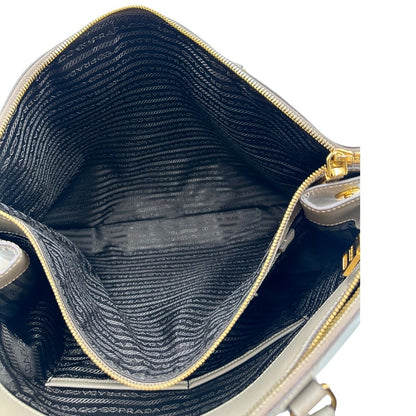 borsa Prada in pelle saffiano color fango con parti metalliche dorate; munita di doppi manici stondati e impreziosita da una clochette portachiavi, di lusso, originale, ottime condizioni.