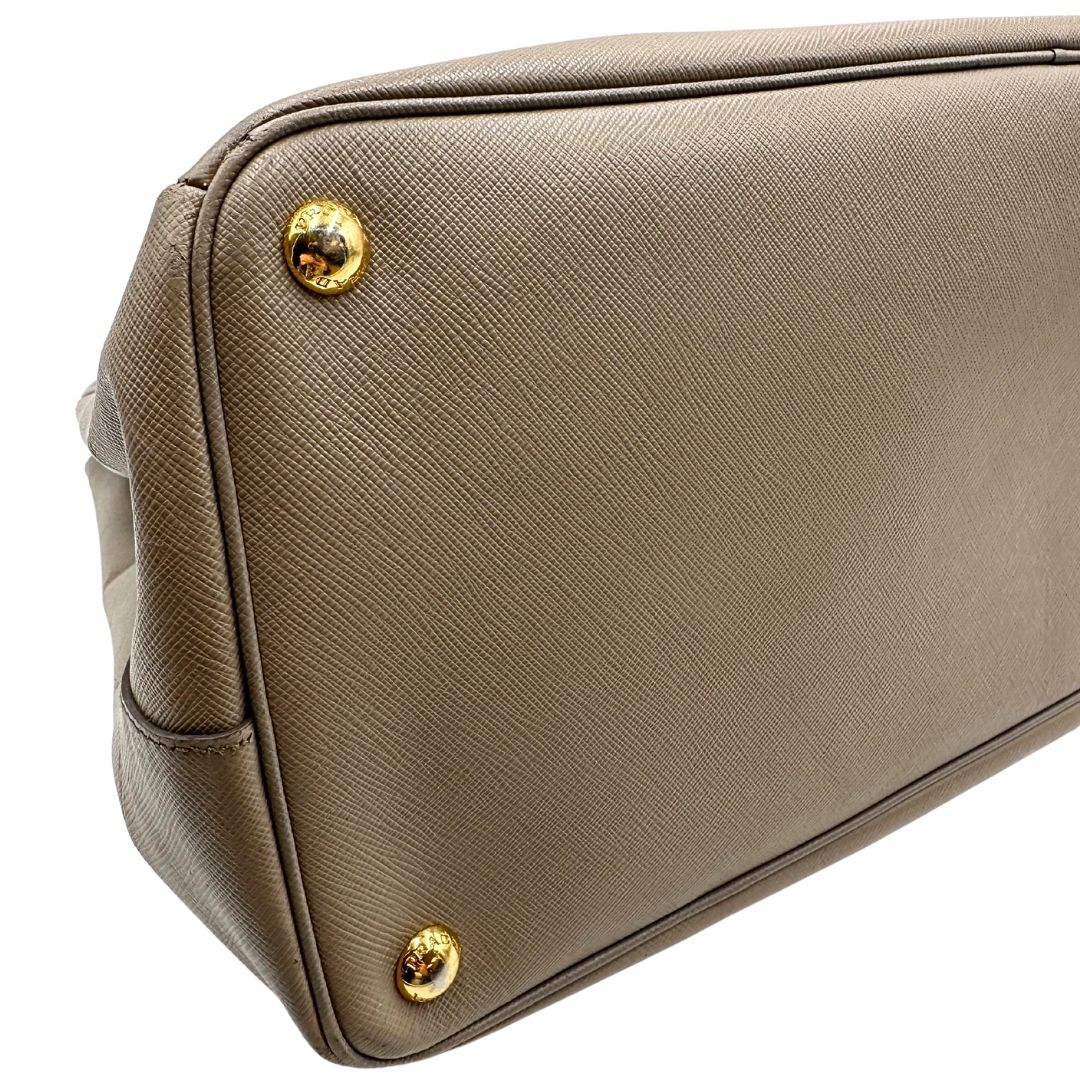 borsa Prada in pelle saffiano color fango con parti metalliche dorate; munita di doppi manici stondati e impreziosita da una clochette portachiavi, di lusso, originale, ottime condizioni.