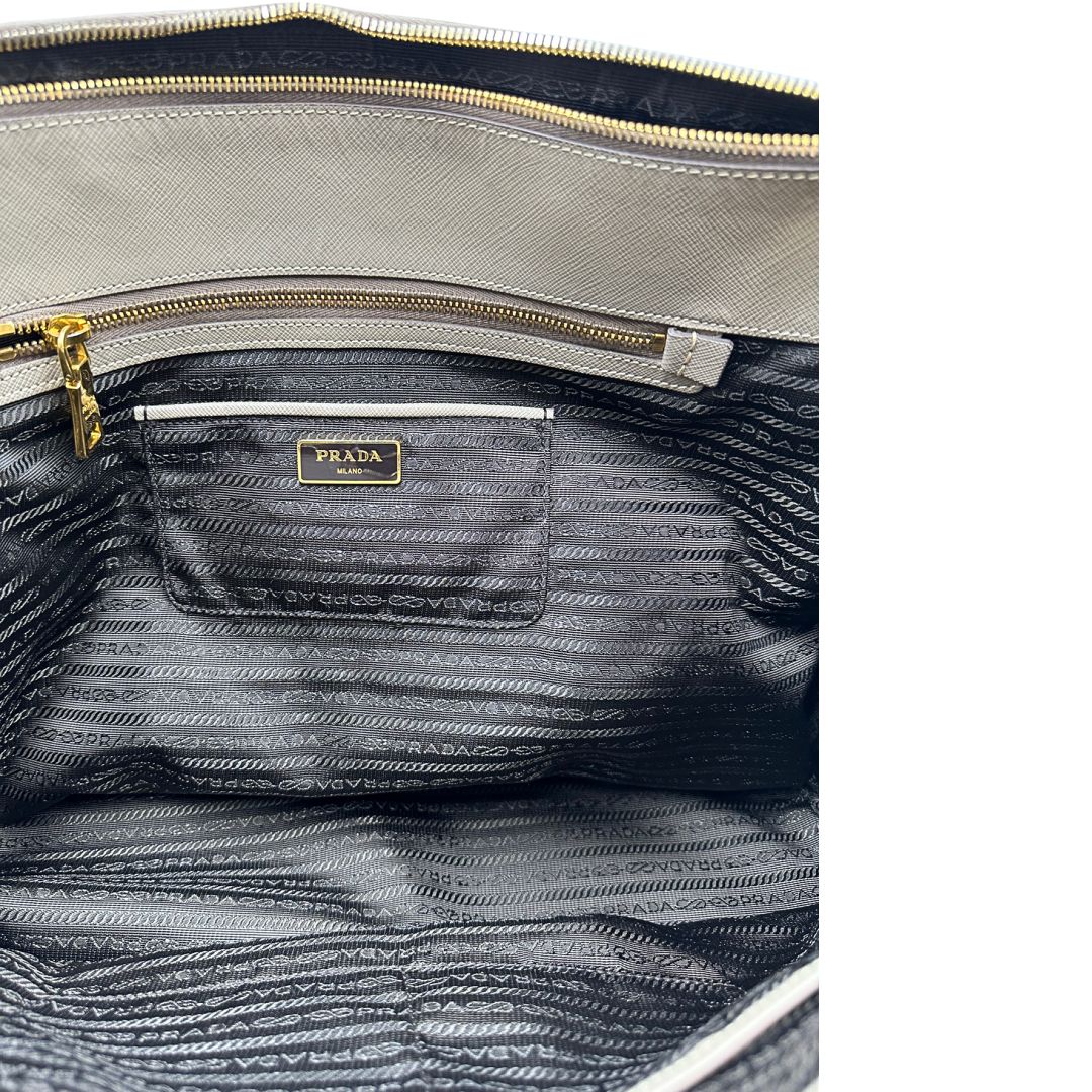 borsa Prada in pelle saffiano color fango con parti metalliche dorate; munita di doppi manici stondati e impreziosita da una clochette portachiavi, di lusso, originale, ottime condizioni.