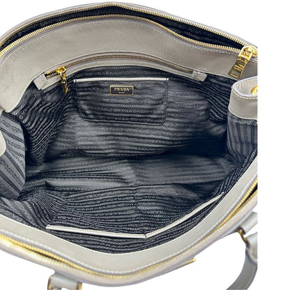borsa Prada in pelle saffiano color fango con parti metalliche dorate; munita di doppi manici stondati e impreziosita da una clochette portachiavi, di lusso, originale, ottime condizioni.