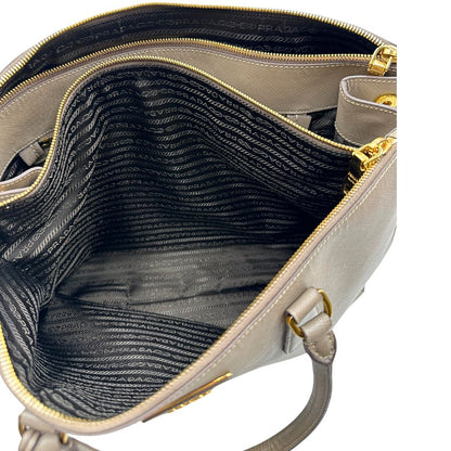 borsa Prada in pelle saffiano color fango con parti metalliche dorate; munita di doppi manici stondati e impreziosita da una clochette portachiavi, di lusso, originale, ottime condizioni.