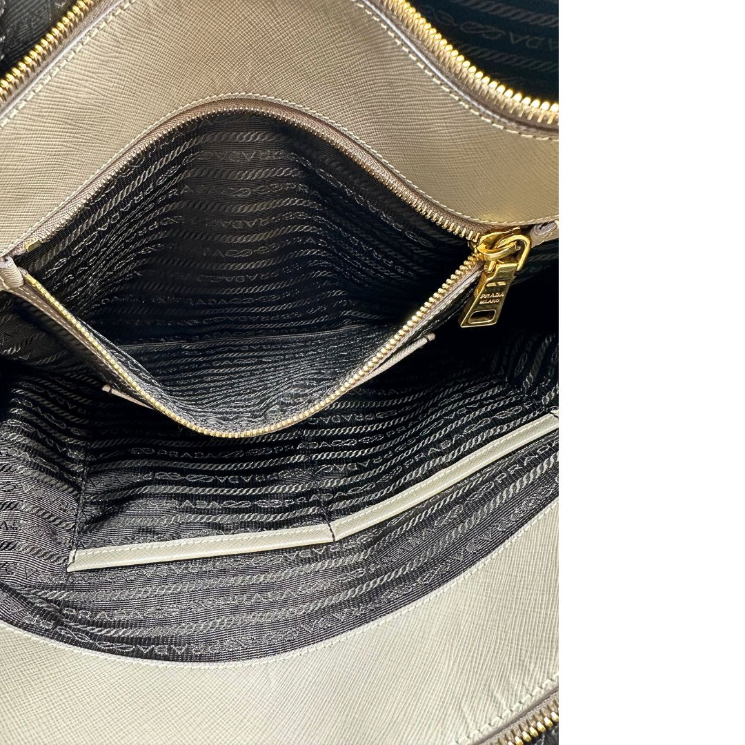 borsa Prada in pelle saffiano color fango con parti metalliche dorate; munita di doppi manici stondati e impreziosita da una clochette portachiavi, di lusso, originale, ottime condizioni.