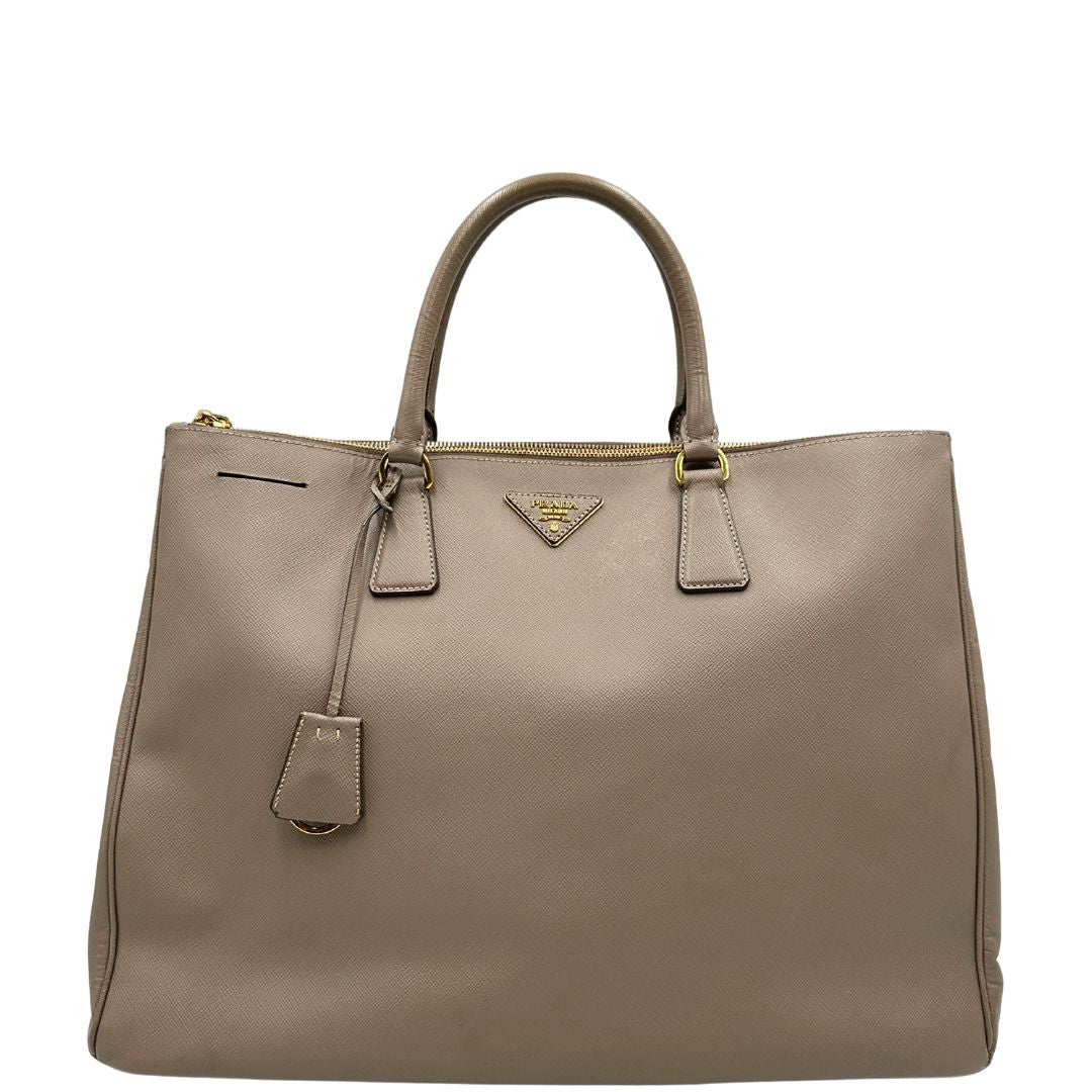 borsa Prada in pelle saffiano color fango con parti metalliche dorate; munita di doppi manici stondati e impreziosita da una clochette portachiavi, di lusso, originale, ottime condizioni.