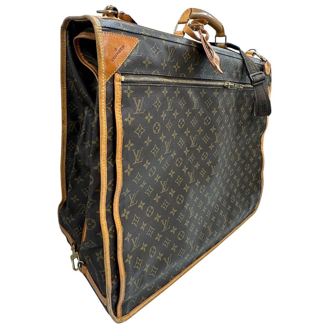 lato Borsa da viaggio in canvas marrone monogram con finiture in vacchetta naturale e parti metalliche dorate; munita di un manico singolo,una tracolla amovibile e regolabile e 5 grucce, di lusso, originale, ottime condizioni. 