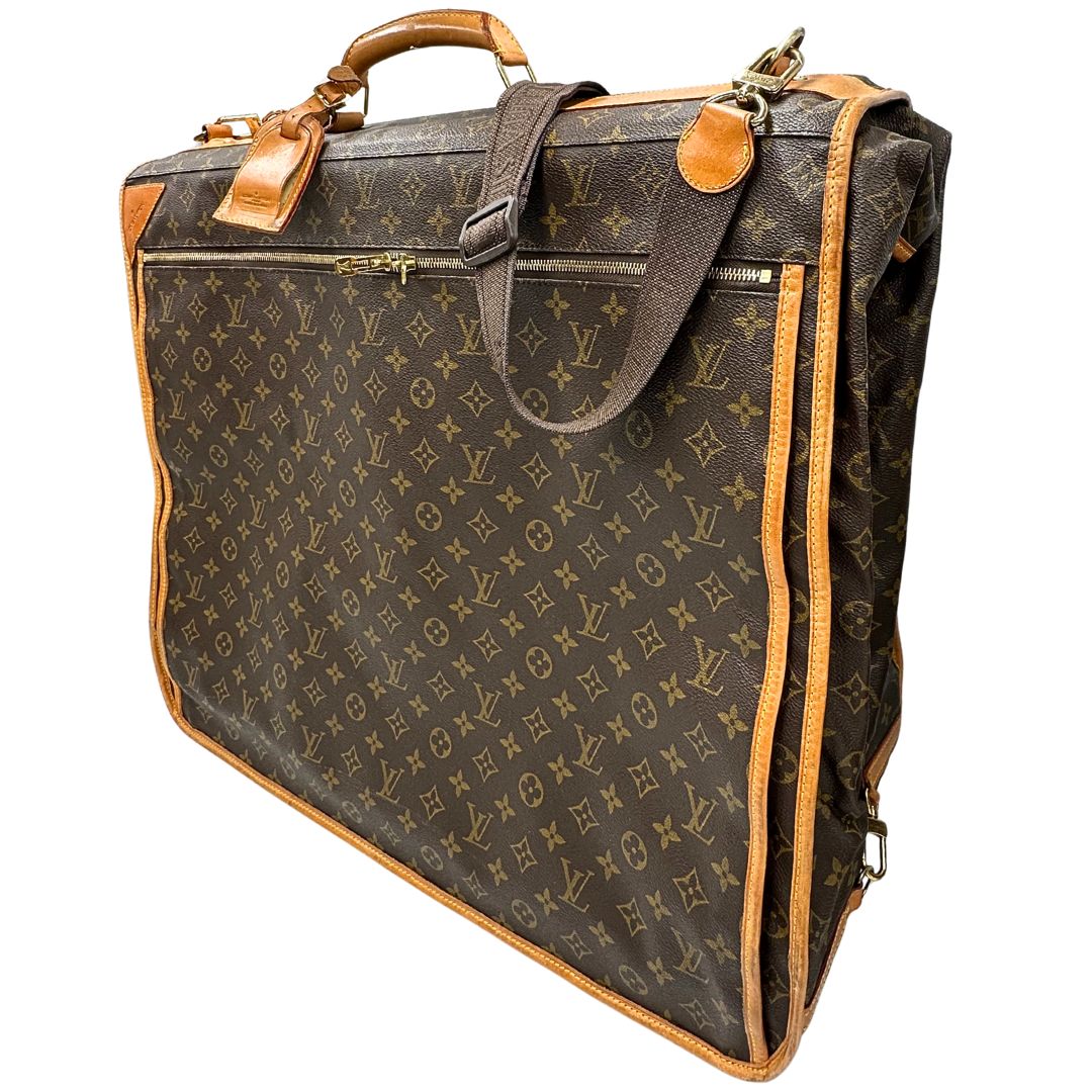 lato Borsa da viaggio in canvas marrone monogram con finiture in vacchetta naturale e parti metalliche dorate; munita di un manico singolo,una tracolla amovibile e regolabile e 5 grucce, di lusso, originale, ottime condizioni. 