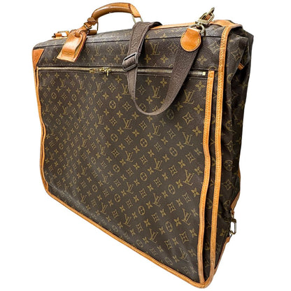 lato Borsa da viaggio in canvas marrone monogram con finiture in vacchetta naturale e parti metalliche dorate; munita di un manico singolo,una tracolla amovibile e regolabile e 5 grucce, di lusso, originale, ottime condizioni. 