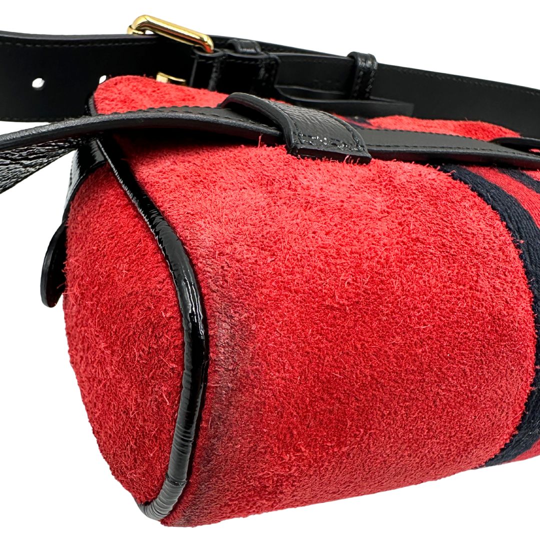 Angolo di un marsupio Gucci Ophidia in pelle scamosciata rossa con finiture in pelle verniciata nera, striscia Web centrale in tessuto blu e rosso, cintura regolabile e amovibile, parti metalliche dorate. Completo di dustbag.