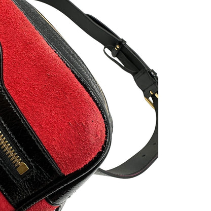Angolo di un marsupio Gucci Ophidia in pelle scamosciata rossa con finiture in pelle verniciata nera, striscia Web centrale in tessuto blu e rosso, cintura regolabile e amovibile, parti metalliche dorate. Completo di dustbag.