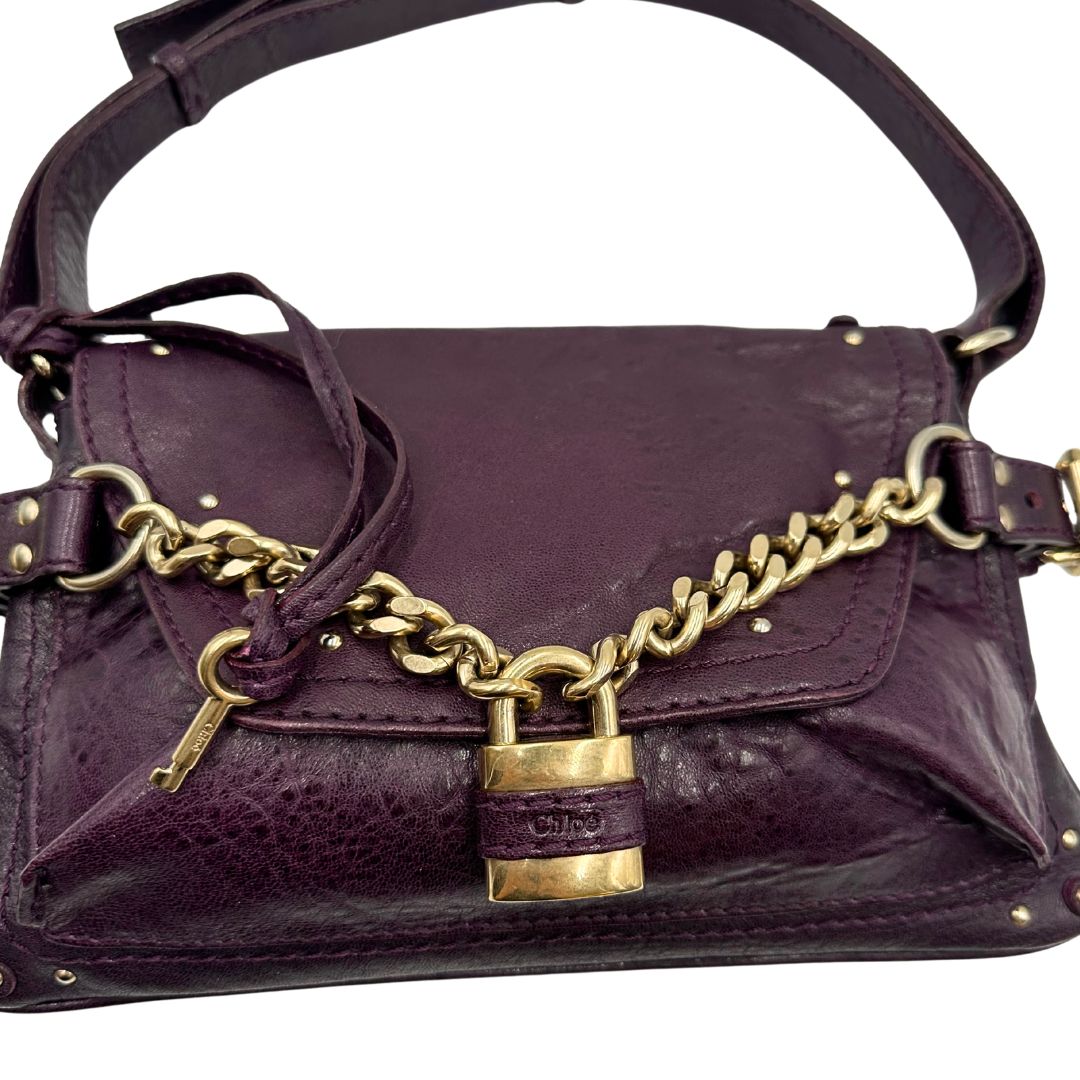Borsa Chloé Maxi Lock in pelle viola prugna con parti metalliche dorate. Munita di un manico regolabile e impreziosita da una catena sul front con lucchetto. Originale, usato, in condizioni ottime. 