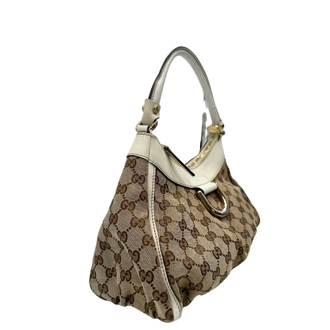 Laterale Borsa Gucci Hobo D-Ring in tessuto beige GG con finiture in pelle bianca e parti metalliche dorate. Munita di un manico in pelle stondato, rifinita con dettaglio D-Ring e logo lettering sul front. Completa di dustbag. Originale, usato, in condizioni ottime. 