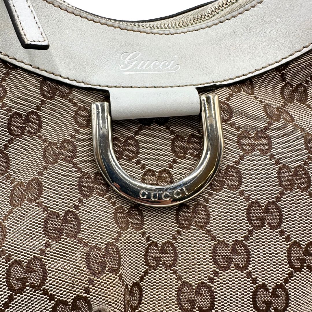 Borsa Gucci Hobo D-Ring in tessuto beige GG con finiture in pelle bianca e parti metalliche dorate. Munita di un manico in pelle stondato, rifinita con dettaglio D-Ring e logo lettering sul front. Completa di dustbag. Originale, usato, in condizioni ottime. 