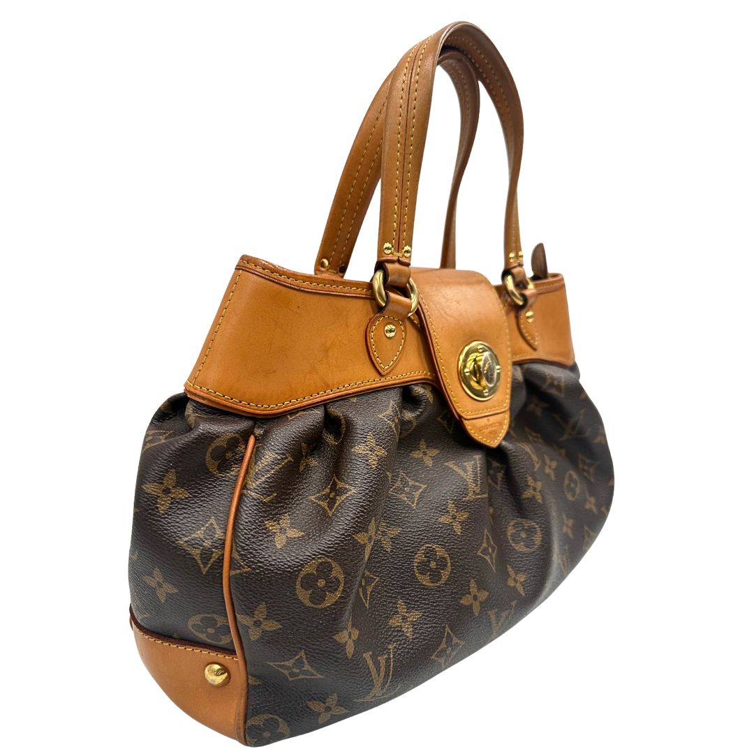 Laterale sinistro di una borsa Louis Vuitton in canvas marrone monogram con finiture in vacchetta naturale e parti metalliche dorate; munita di doppi manici stondati, da indossare a mano.