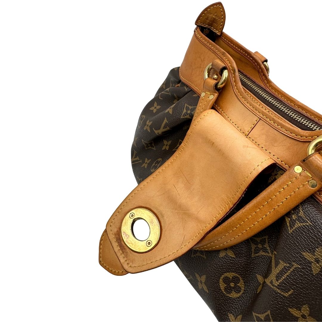 Patta di chiusura di una borsa Louis Vuitton in canvas marrone monogram con finiture in vacchetta naturale e parti metalliche dorate; munita di doppi manici stondati, da indossare a mano.