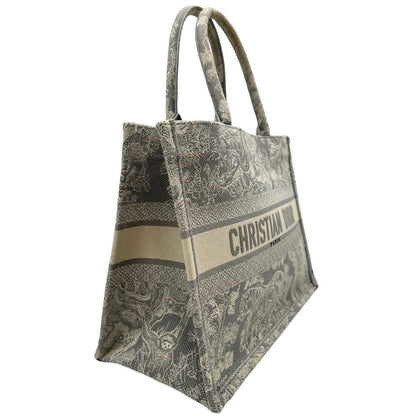 Laterale sinistro di una borsa tote CD in tessuto grigio e écru con ricamo Toile De Jouy. Da indossare a mano. Completa di dustbag.