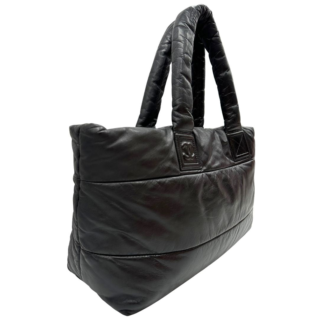 Laterale sinistro di una borsa Chanel in pelle effetto imbottito nera, con metalleria argentata. Da indossare a spalla.