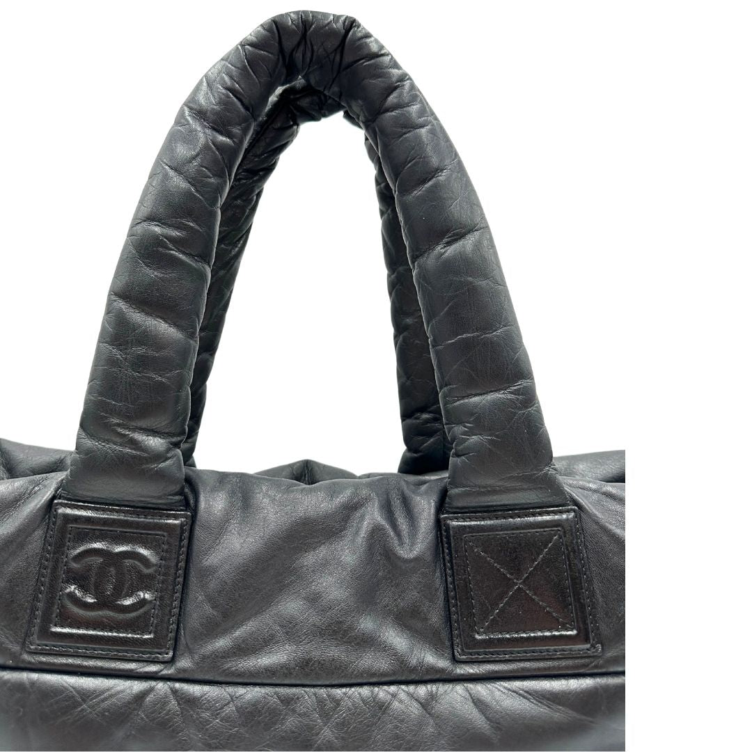 Manici di una borsa Chanel in pelle effetto imbottito nera, con metalleria argentata. Da indossare a spalla.