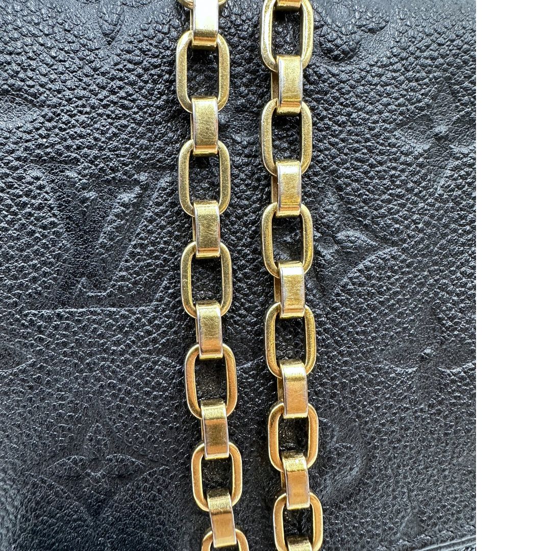 Dettagli catene di una borsa Louis Vuitton in pelle nera monogram Empreinte con parti metalliche dorate; munita di una tracolla scorrevole in catena. Indossabile a spalla e a tracolla.