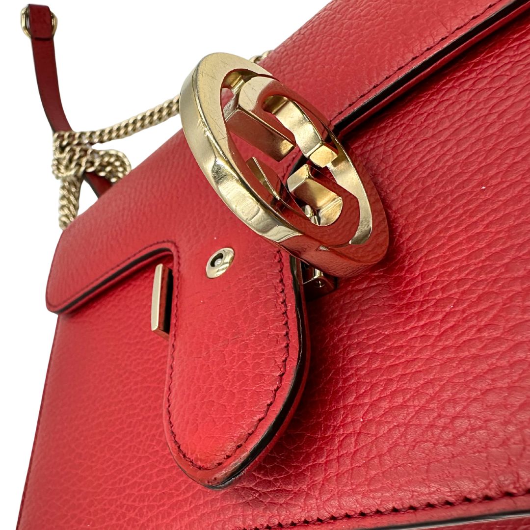 Chiusura di una borsa Gucci Interlocking in pelle martellata rossa con parti metalliche dorate. Munita di una tracolla scorrevole in catena non amovibile e spallaccio in pelle. Chiusura con doppie G incrociate. Completa di dustbag. Indossabile a spalla o a tracolla.