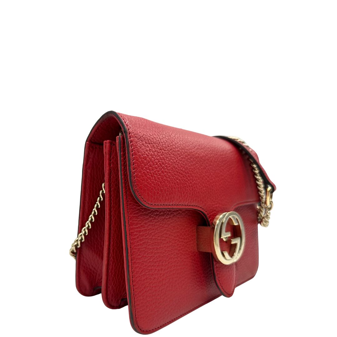 Laterale sinistro di una borsa Gucci Interlocking in pelle martellata rossa con parti metalliche dorate. Munita di una tracolla scorrevole in catena non amovibile e spallaccio in pelle. Chiusura con doppie G incrociate. Completa di dustbag. Indossabile a spalla o a tracolla.