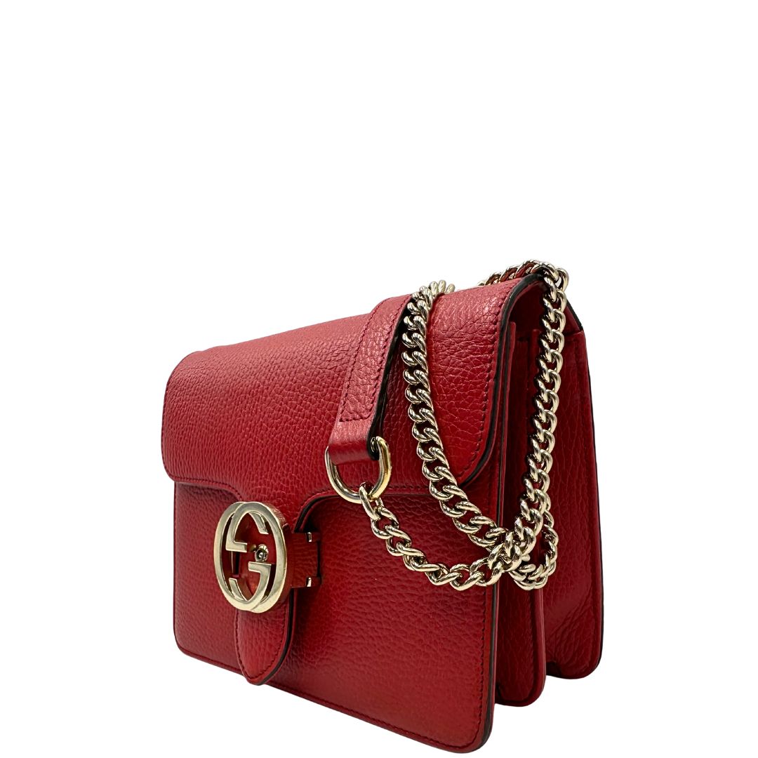 Laterale destro di una borsa Gucci Interlocking in pelle martellata rossa con parti metalliche dorate. Munita di una tracolla scorrevole in catena non amovibile e spallaccio in pelle. Chiusura con doppie G incrociate. Completa di dustbag. Indossabile a spalla o a tracolla.